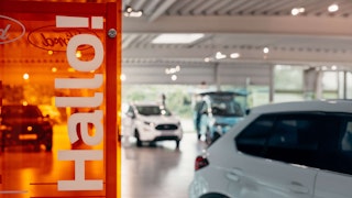 Willkommen im Ford Autohaus – moderne Ausstellungsfläche mit vielfältiger Fahrzeugauswahl. Innenansicht eines Ford Autohauses mit „Hallo“-Schild und ausgestellten Fahrzeugen.