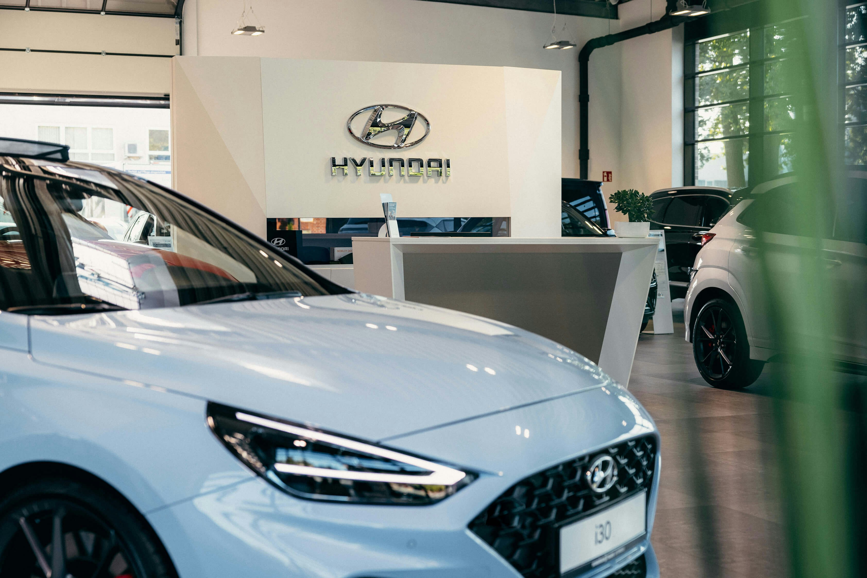 Hyundai Service mit Empfangsbereich und Fahrzeugausstellung Heller Empfangsbereich beim Hyundai Service mit mehreren ausgestellten Fahrzeugen und dem Hyundai Logo im Hintergrund