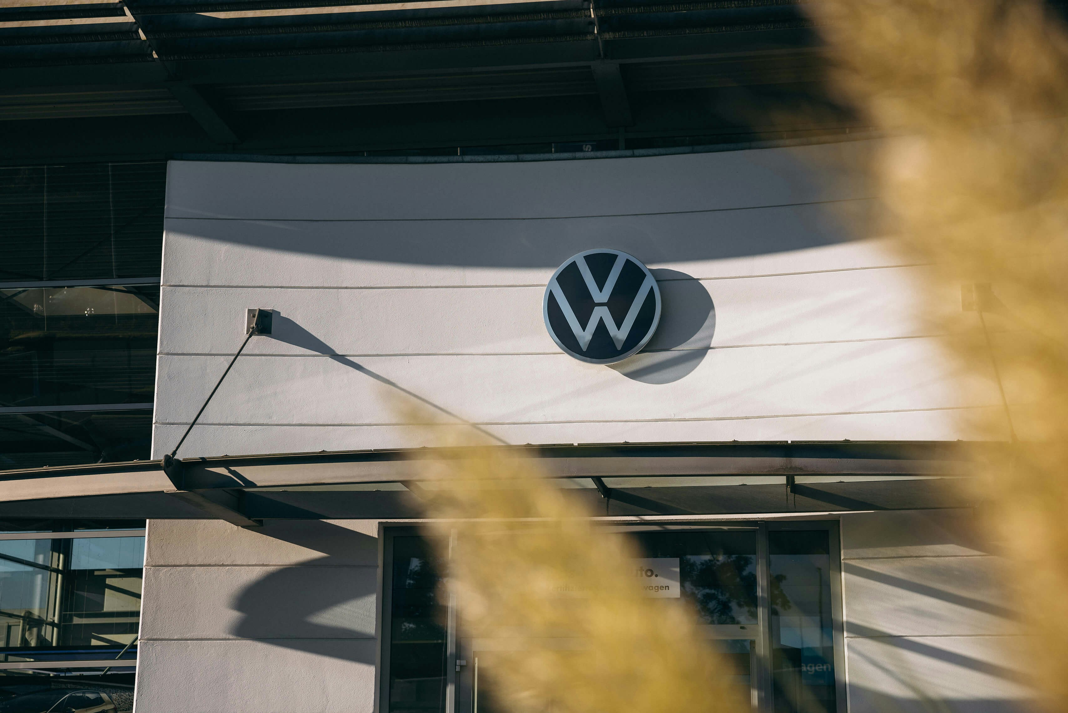 VW Autohaus – modernes Markenlogo an der Außenfassade VW Autohaus mit Volkswagen Logo an Gebäudefront im Sonnenschein