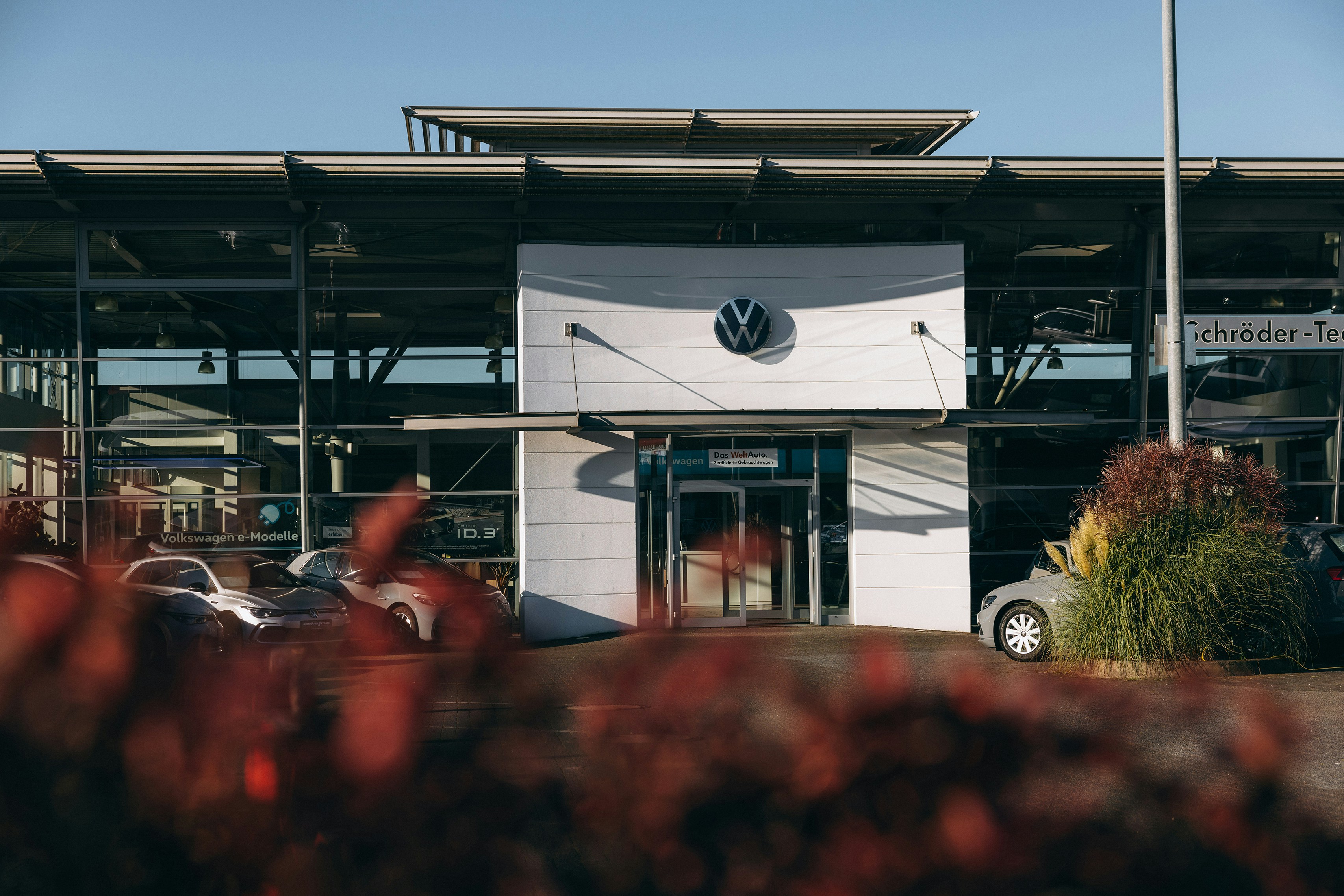 VW Autohaus mit Glasfassade und Eingangsbereich bei Sonnenschein Außenansicht eines Volkswagen Autohauses mit Glasfront, VW-Logo über dem Eingang