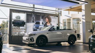 VW Jahreswagen im Autohaus Ein weißes VW T-Roc Cabriolet steht als Jahreswagen in einem modernen Showroom mit großer Werbewand im Hintergrund