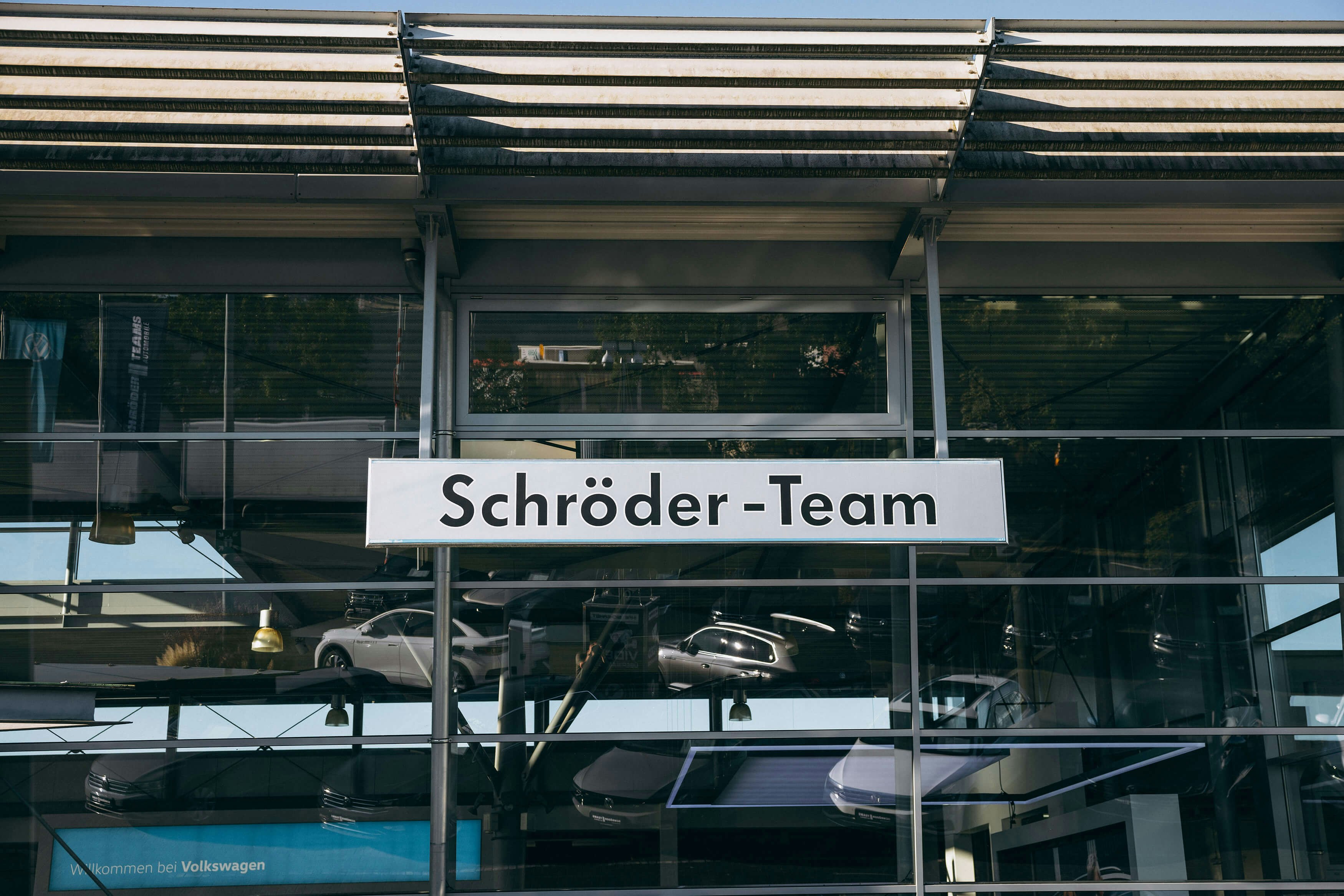 VW Autohaus Schröder Team – Standortansicht mit Glasfassade Außenansicht des VW Autohauses Schröder Team mit moderner Glasfassade und reflektierten Fahrzeugen im Schaufenster