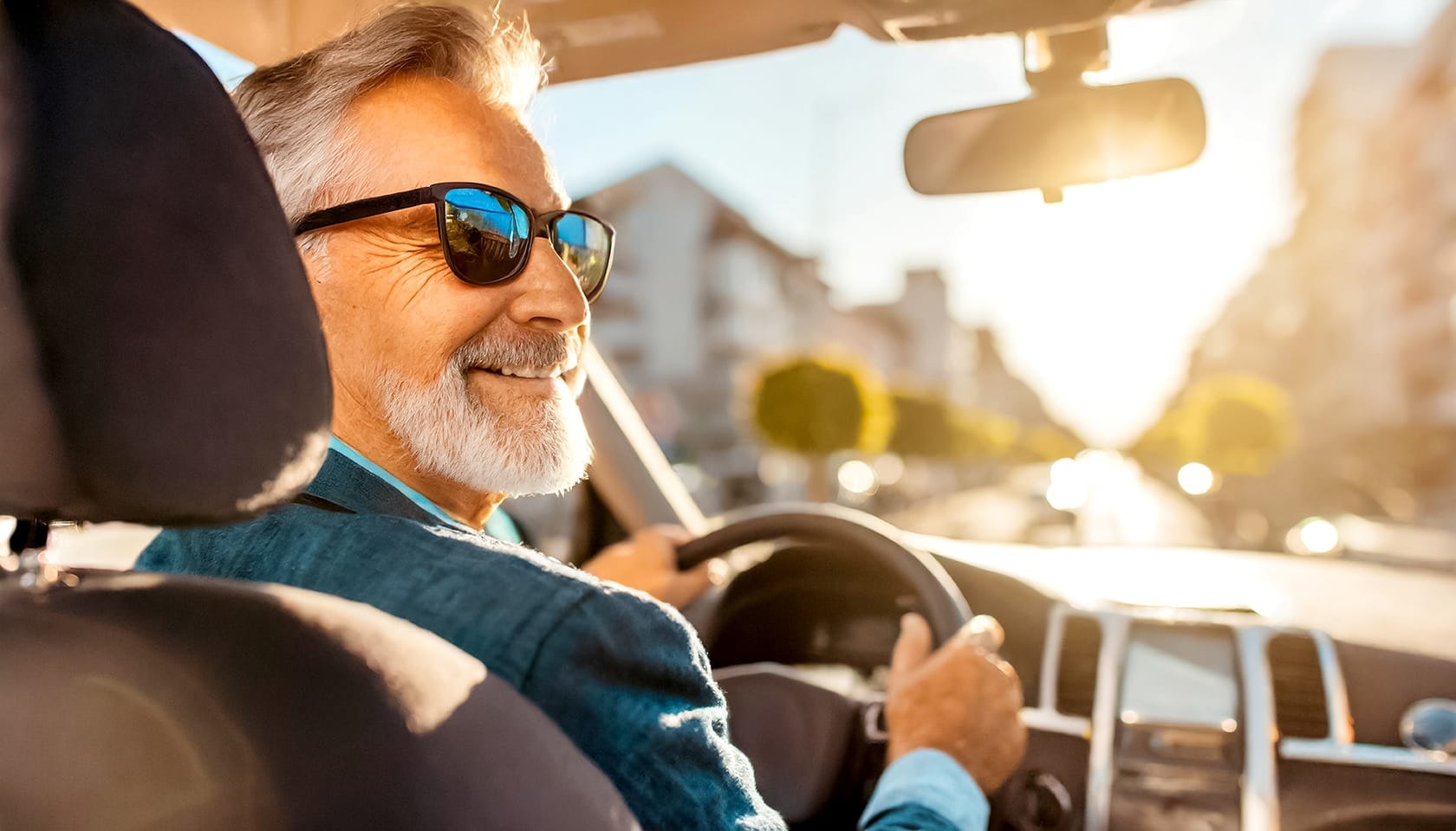 Mit Erfahrung ans Ziel – unterwegs mit Leidenschaft fürs Fahren. Ein freundlicher Taxifahrer mit Sonnenbrille sitzt lächelnd am Steuer seines Fahrzeugs, während die Sonne durch die Windschutzscheibe scheint.