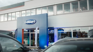 Eingangsbereich des Ford-Autohauses mit großem Markenlogo Haupteingang zur Ford-Verkaufshalle mit großem Logo über dem Eingang und Autos im Vordergrund